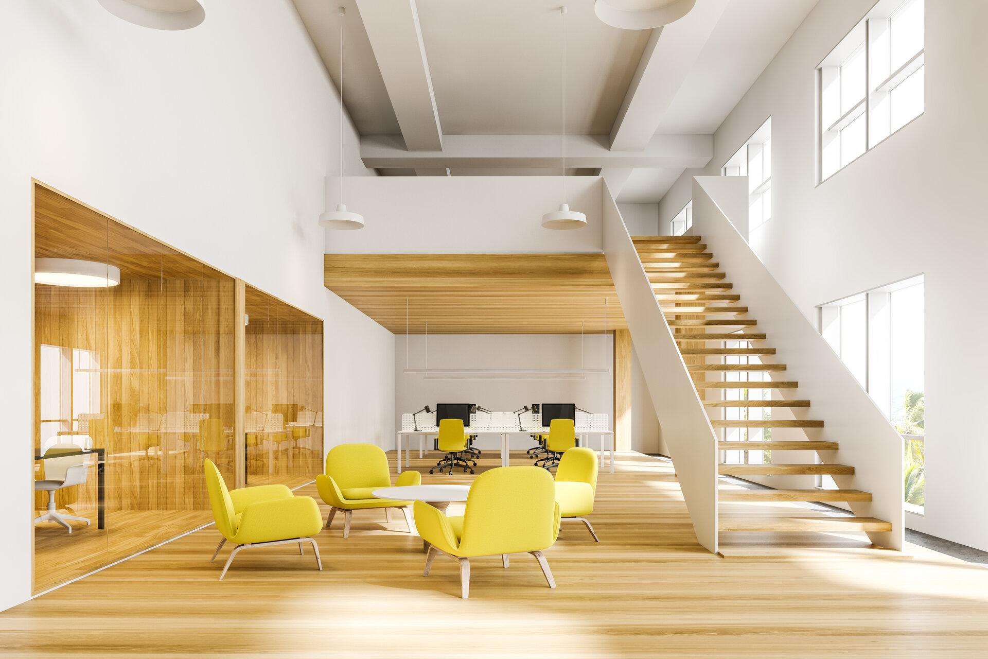Innenraum eines hellen zweistöckigen Büros mit weißen und hölzernen Wänden und Holztreppe, einem komfortablen Wartezimmer mit gelben Sesseln und Open-Space-Bereich im Hintergrund.