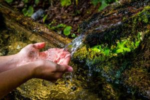 Sich waschende Hände aus einer Quelle mit klarem Wasser