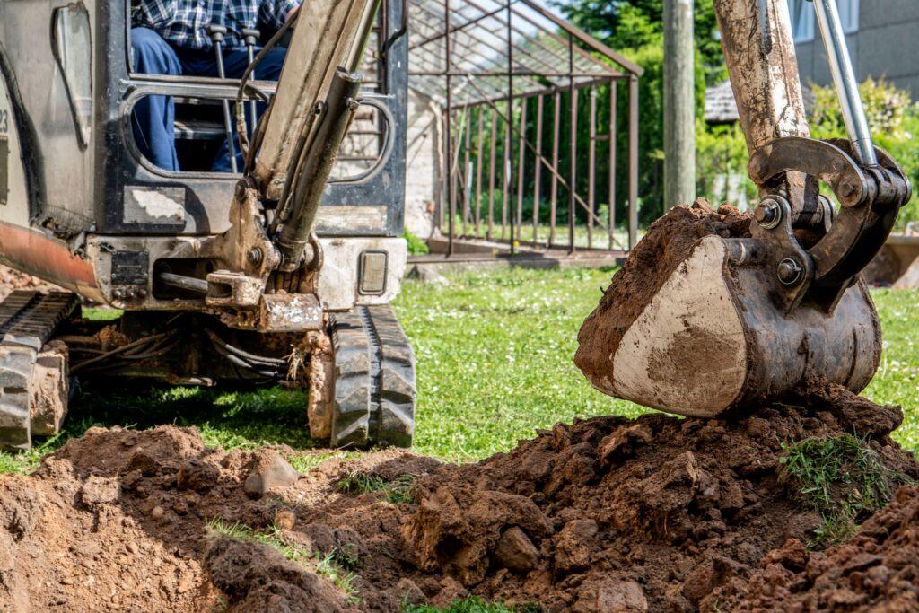 Bagger hebt Erdmaterial bei Gartenarbeiten